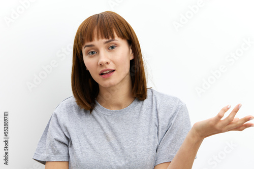 a beautiful, sweet, attractive woman stands on a white background in light clothes and spreads her hands in surprise. Horizontal photo with an empty space for inserting an advertising layout