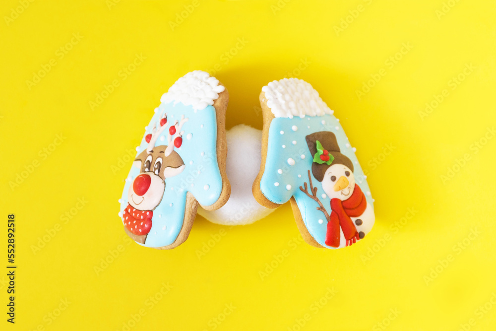 Two colorful Christmas biscuits in the shape of gloves holding a snowball against yellow background. Minimal surreal concept for winter season banner or print. Design for season greetings card.