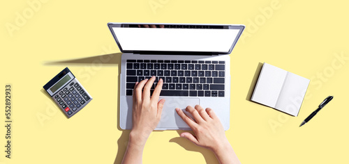 Person using a laptop computer with a notebook and a calculator - flat lay