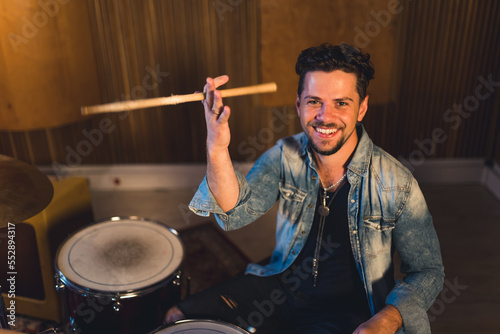 medium shot of a young drumer man holding drums sticks and smiling widely, musical band concept musical studio. High quality photo photo