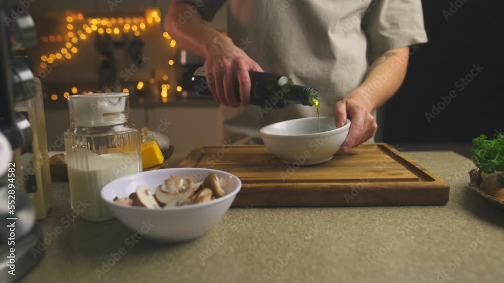 Video. A young man prepares a festive family dinner, dinner in the home kitchen. Pours olive oil into a bowl. Mushrooms, cheese, milk in a jug are on the table nearby. Simple and delicious recipes. Video. A young man prepares a festive family dinner, dinner in the home kitchen. Pours olive oil into a bowl. Mushrooms, cheese, milk in a jug are on the table nearby. Simple and delicious recipes.