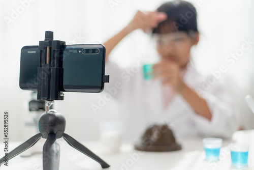 Asian school girl making easy chemistry experiments and recording a video for his followers, Young blogger kid posing in front of camera for vlog, Children make vlog for social media channel concept.