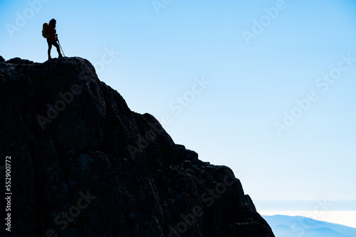 Silhouette of a successful hiker at the edge of the cliff, staring at the horizon