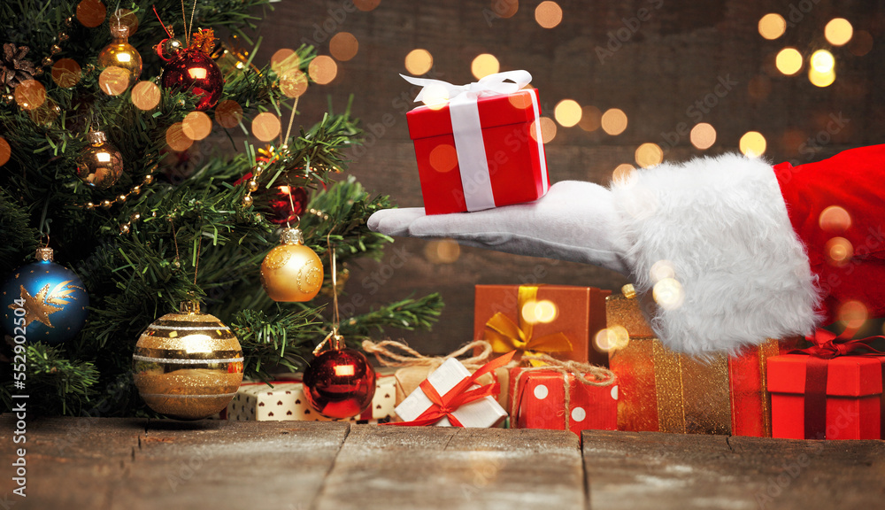 Obraz premium Santa Claus hand holding a wrapped Christmas present.