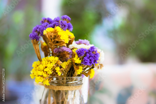 A bouquet of colorful dried field yellow, purple statica limonium sinuat flowers in a glass vase, jar. Cute floral still life on a blurry natural background in summer. Cute pretty flower composition.  photo