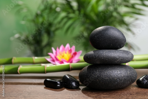 Stacked spa stones  bamboo stems and flower on wooden table against blurred background. Space for text