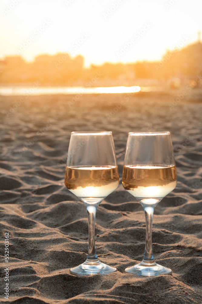 Glasses of tasty wine on sand near sea