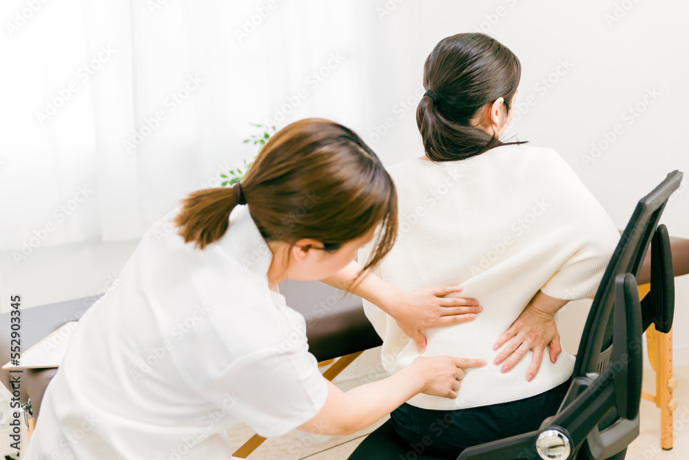 Fototapeta premium 腰痛・脊椎の痛みで整体院・整骨院で施術を受けるアジア人女性医師・理学療法士・看護師と患者