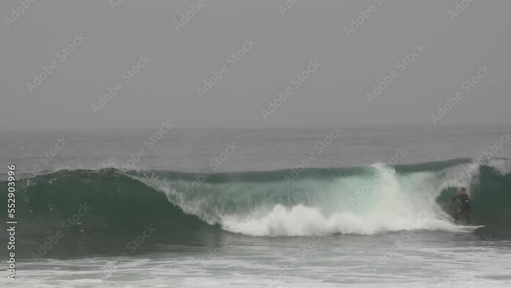 A surfer paddling and catching a wave and rides out of frame towards the right. Camera stand still. Recorded in 4k quality in a cloudy morning in Lima, Peru. A surfer paddling and catching a wave and rides out of frame towards the right. Camera stand still. Recorded in 4k quality in a cloudy morning in Lima, Peru.