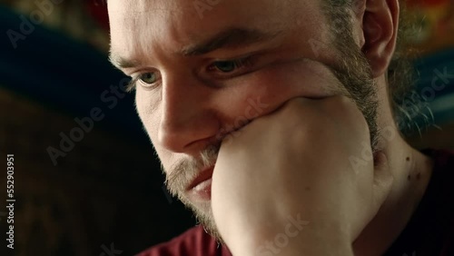 Static close up of a young bearded man staring, focused and consentrated down on desk while leaning head on arm. Static. photo