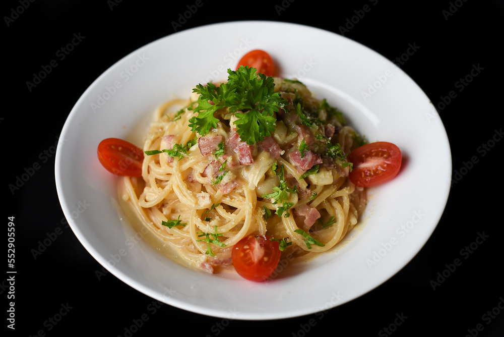 Pasta carbonara with bacon on white plate isolated on black background side view 
