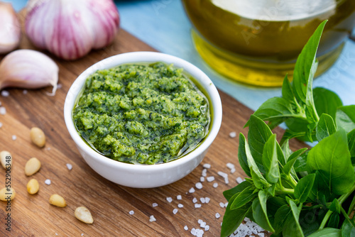 ingredients for the preparation of pesto sauce. basil, pine nuts, garlic, basil, parmesan on a blue table and wooden board, close-up