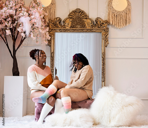 Two Black women sitting on bench chatting and laughing in front of mirror