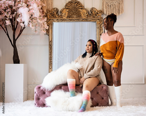 Two Black women sitting and standing in front of mirror, wearing long  socks