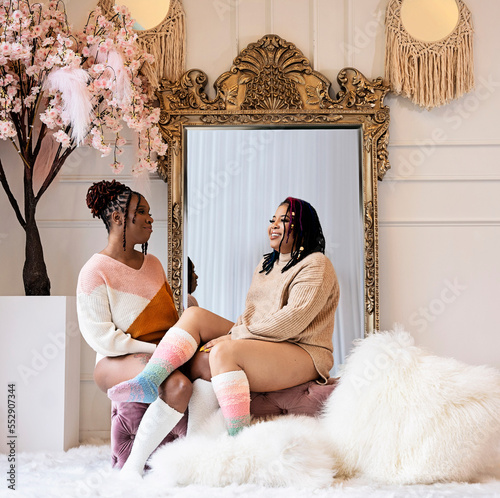 Two Black women sitting on bench chatting and laughing in front of mirror
