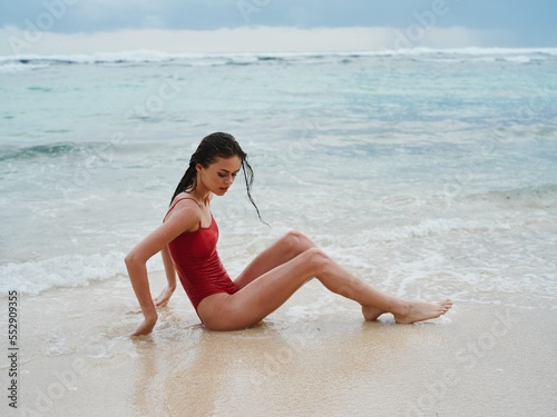 Woman with wet hair after swimming in the ocean in a red swimsuit lies sexily on the beach in Bali  travel to Indonesia 