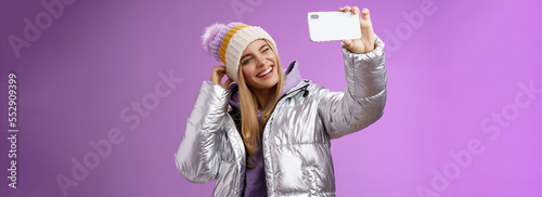 Joyful carefree charming blond girl having fun wanna post pictures from ski resort vacation taking seflie holding smartphone mimicking show tongue winking look mobile display, purple background photo