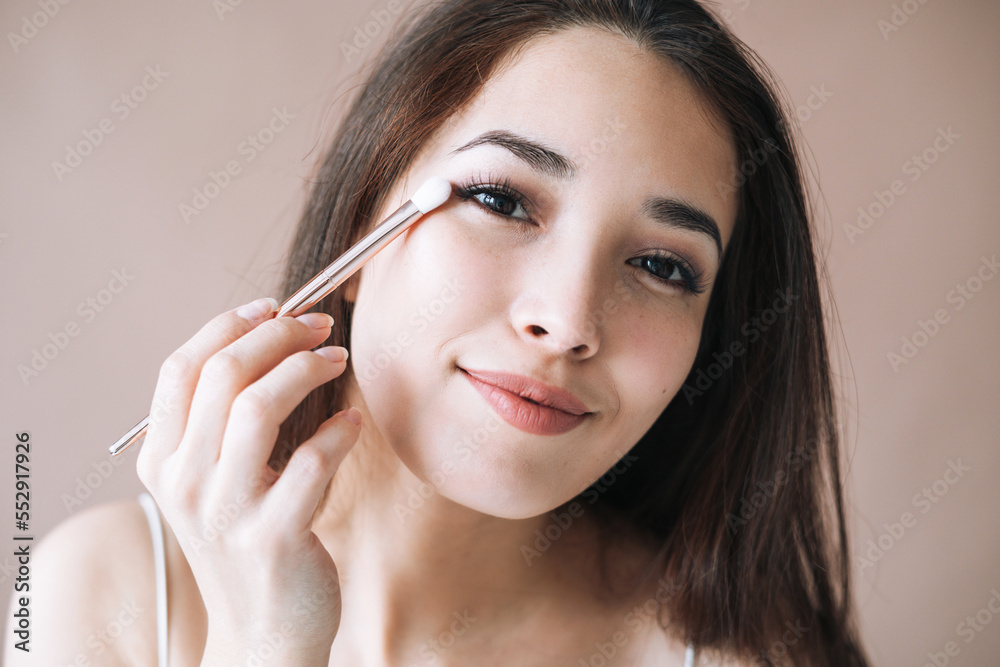 Portrait of young asian woman with makeup brush on beige background Portrait of young asian woman with makeup brush on beige background
