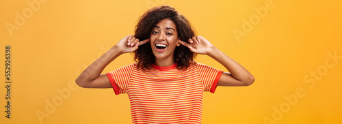 Do not care what saying cannot hear you. Carefree indifferent good-looking african american woman with curly hairstyle closing ears with index finger singing lalala during argument behaving childish