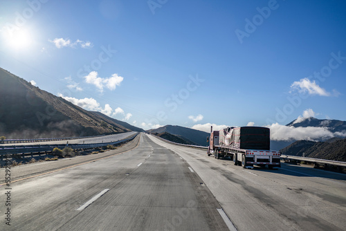 фотографія Heavy duty classic red big rig semi truck transporting covered cargo on flat bed