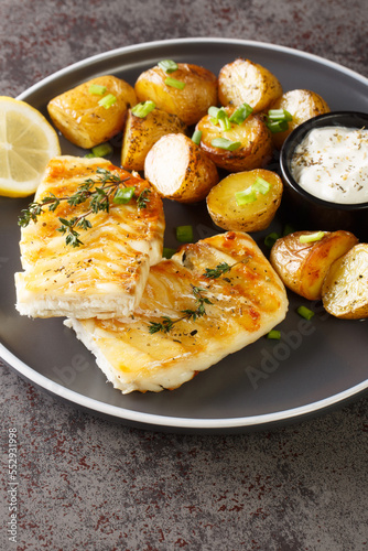Healthy food serving grilled fish cod with baked potatoes, sauce and lemon close-up in a plate on the table. Vertical