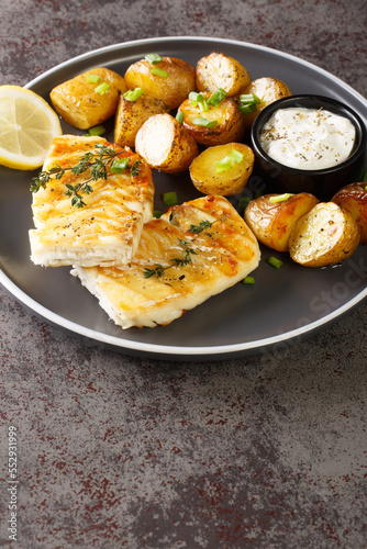 grilled cod fish with baked jacket potatoes, cream sauce and lemon close-up in a plate on the table. Vertical