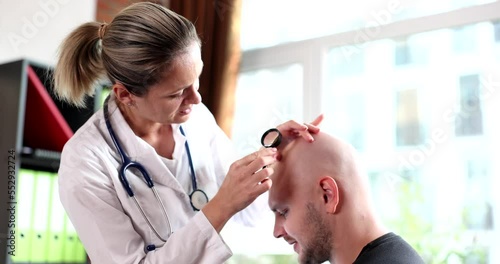 Trichologist with magnifying glass examines bald patient with alopecia in clinic photo