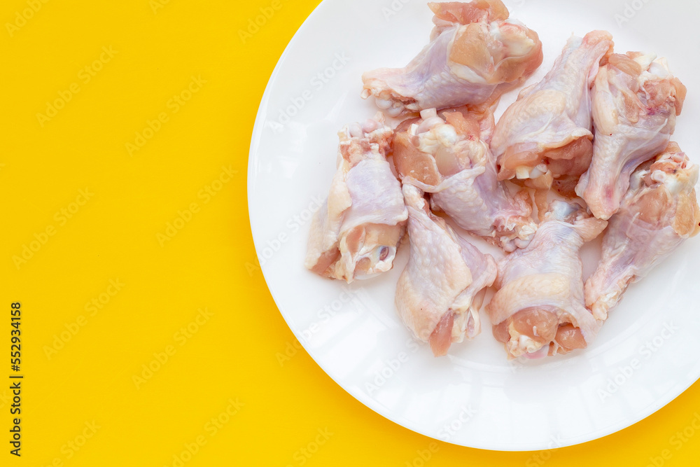 Fresh raw chicken wings (wingstick) in white plate on yellow background.