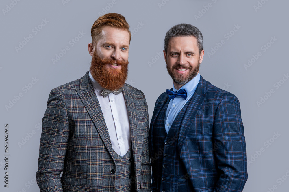 smiling tuxedo men in menswear isolated on grey background. two men in tuxedo menswear. smiling tuxedo men in menswear isolated on grey background. two men in tuxedo menswear.