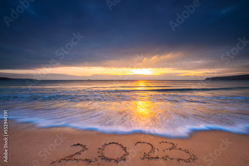 Happy New Year 2023 travel, sport, meditation concept, text lettering on the ocean beach sand at sunrise. Sea Sunset of 2022.