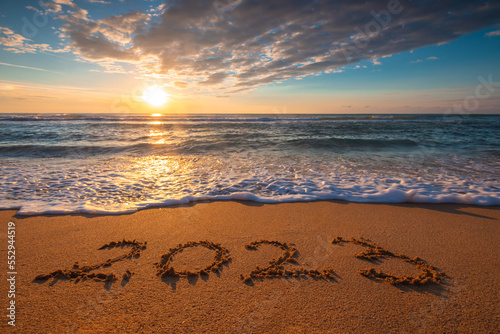 Ocean beach sunrise and text Happy new year 2023 on coast sand. Sea sunset.