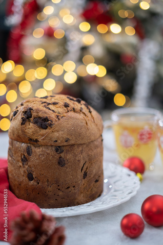 Chocolate chips Panettone and cups of tea in white table with red festive balls and bokeh background. High quality photo