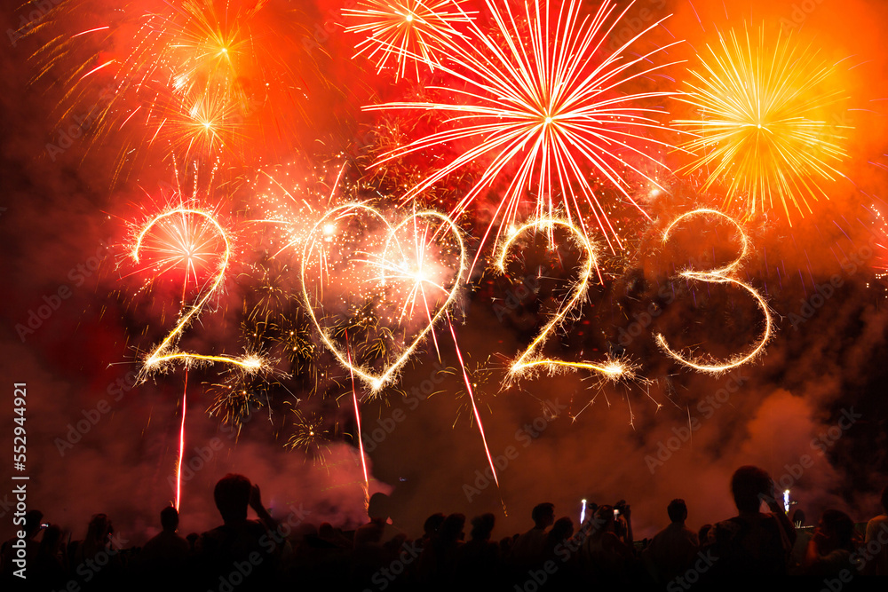 Obraz premium 2023 new year text made with fireworks sparklers and bengal lights on night sky at midnight. Crowd of People celebrate, concert stage and hands up in the air