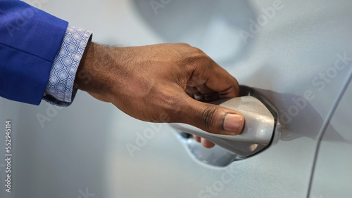 Salesman hand opens car to show customer nice interior of white vehicle. Black dealer tries to intrigue and help customer decide on purchase