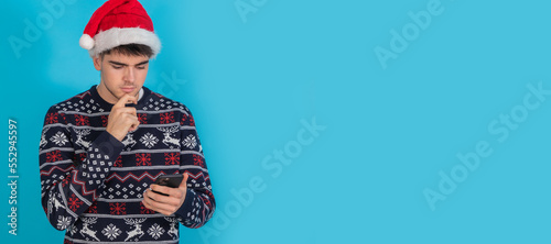 isolated young man in christmas clothes and santa claus hat with mobile phone or smartphone