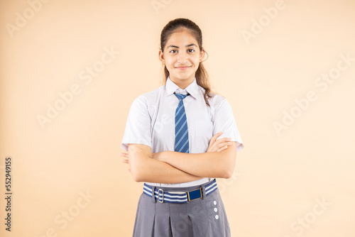 Fotografie Happy confident Indian student schoolgirl wearing school uniform standing cross arm isolated over beige background, Studio shot, closeup, Education concept
