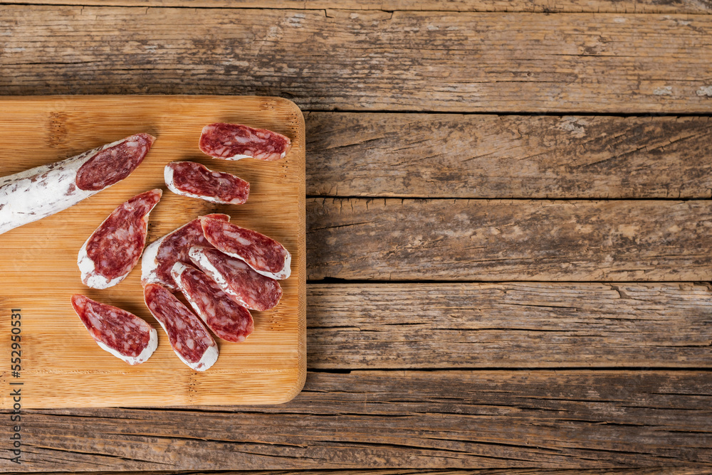 Fuet, typical Catalan sausage spread throughout Spain based on pork and bacon, cut into slices on a wooden cutting board, top view.