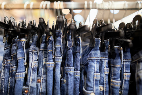 Many blue jeans hang on a rack. Close-up of jeans hanging in the store. Jeans or denim pants hanging on a hanger in a clothing store. The concept of shopping, selling and denim fashion. soft focus
