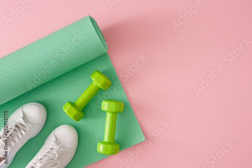 Fitness accessories concept. Creative composition of dumbbells, green exercise mat and white sports shoes on pastel pink background. Flat lay with copy space. Minimal sport idea.