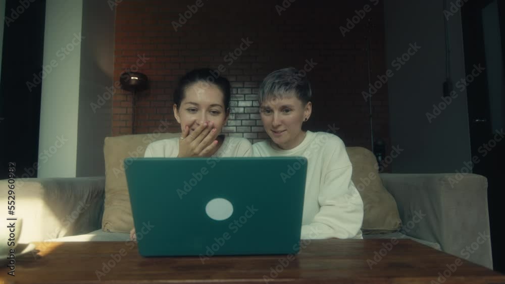 Two young women watching funny videos on their laptops while relaxing together at home Two young women watching funny videos on their laptops while relaxing together at home