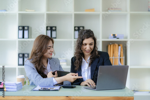 Young attractive caucasian boss and assistant listening financial business consulting with graph paper and tablet laptop on table in office