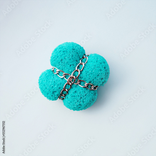 A sponge tied with chains, minimal creative concept against white background with soft shadow.