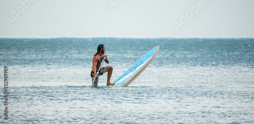 Sea man sup. Asian athlete man swimming in sea and paddleboarding at summer sunset. Healthy strong male enjoy outdoor active lifestyle and water sports on holiday vacation. © panophotograph