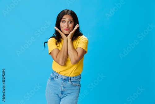 Woman in yellow t-shirt on blue background posing gestures emotions and signals with smile, hands up happiness copy space
