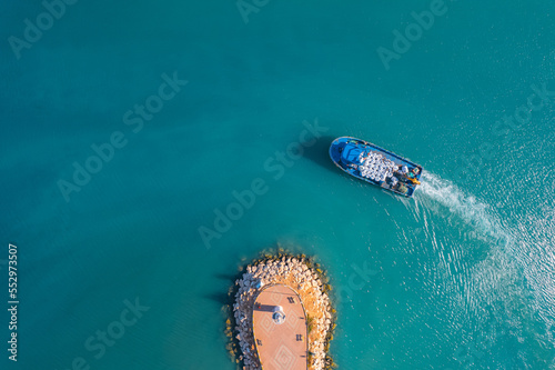 Small cargo ship sails through blue sea to serve fish farm, aerial top view © Parilov