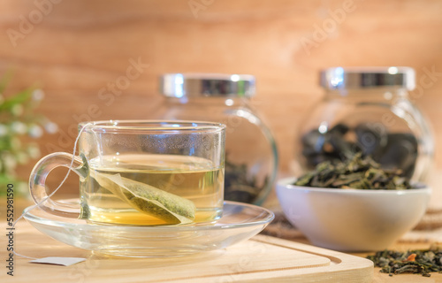 Glass cup of healthy green tea on wooden board with soft sunlight shining into a warm atmosphere.