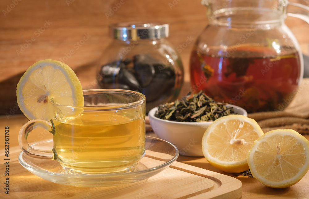 Warm cup of tea with lemon, teapot, dried green tea leaves on wooden desk at morning. Warm cup of tea with lemon, teapot, dried green tea leaves on wooden desk at morning.