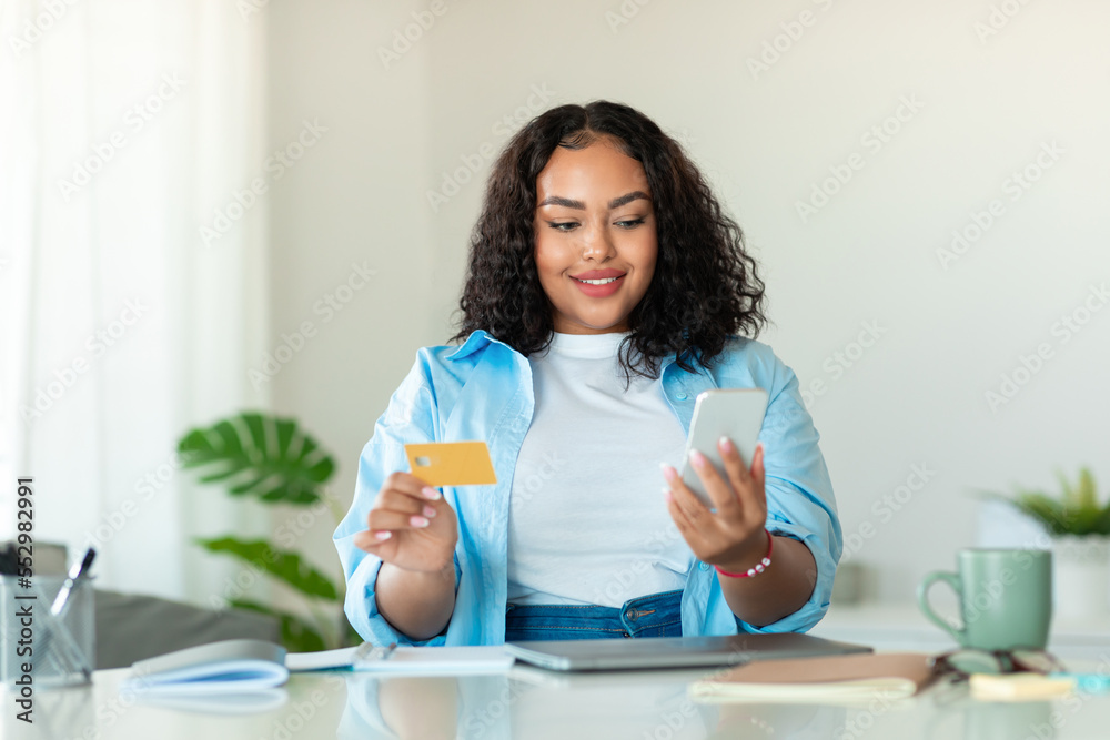 Young african american chubby woman using mobile phone and credit card, checking new app for online shopping Young african american chubby woman using mobile phone and credit card, checking new app for online shopping