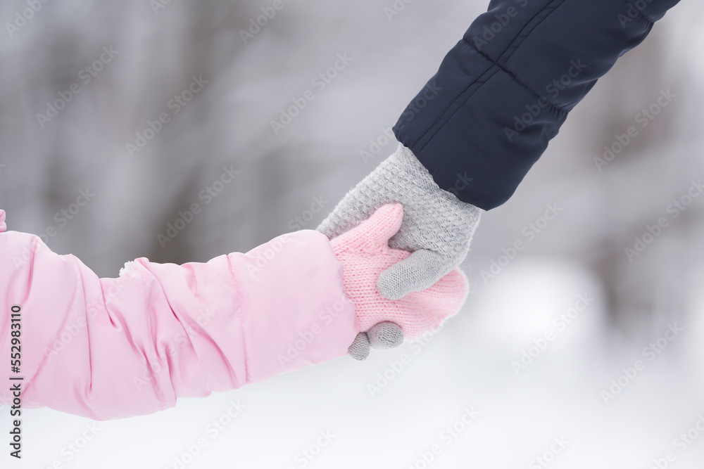 © fotoduets - Little daughter and young adult mother holding each other hands in warm gloves on nature background. Walking and spending time together in cold winter day. Closeup. Back view. © fotoduets - Little daughter and young adult mother holding each other hands in warm gloves on nature background. Walking and spending time together in cold winter day. Closeup. Back view.