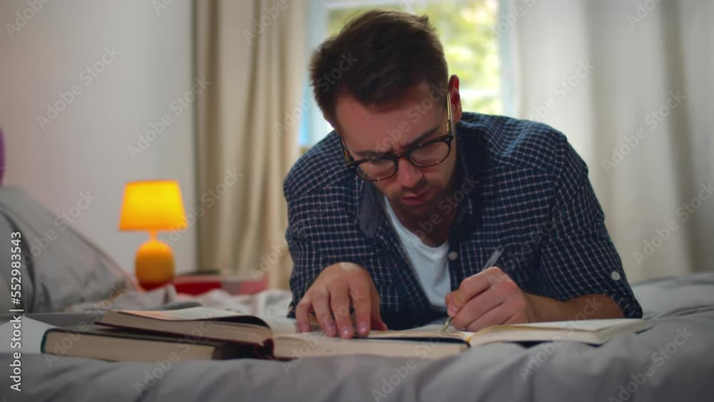 Young man reads books lying on bed. Realtime